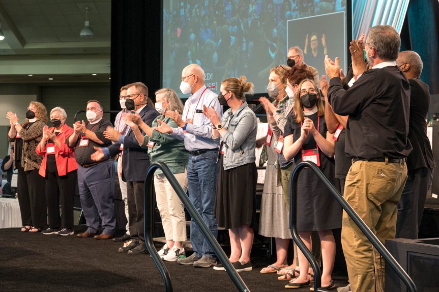 A line of masked deputies on a raised platform facing the room and clapping