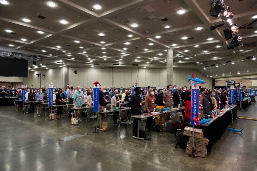 Hundreds of delegates gathered in a large conference center room stand as they are able before their tables, marked by their deputation poles indicating their oioceses of origin. The mood appears somber because everyone is masked, but the atmosphere was at once mournful, celebratory, and tearful.